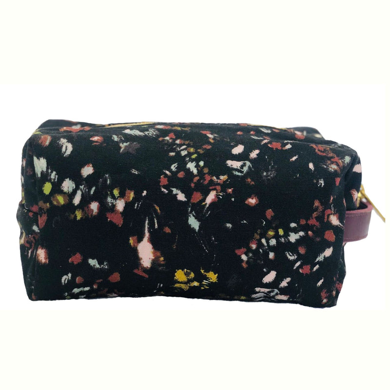 Floral-patterned cosmetic pouch with a purple logo patch and zipper, featuring a black base with red, yellow, and white accents, back view