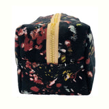 Floral-patterned cosmetic pouch with a gold zipper, featuring a black base with red, yellow, and white accents, end view