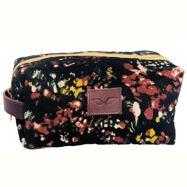 Floral-patterned cosmetic pouch with a purple logo patch and zipper, featuring a black base with red, yellow, and white accents